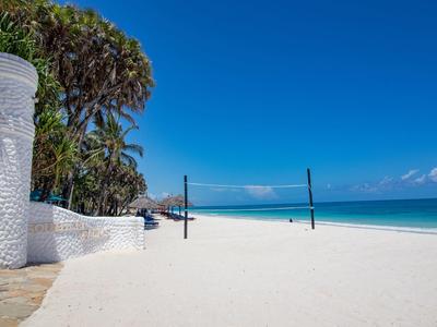 Prázdná písečná pláž s volejbalovou sítí a jasně modrou oblohou u moře.