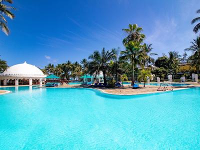 Velký hotelový bazén s palmami a slunečníky pod modrou oblohou.