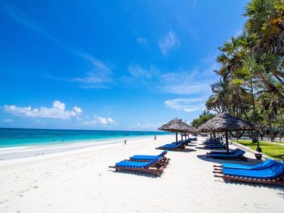 Strand mit blauen Liegen und Strohhüttchen unter Palmen an klarem Himmel.
