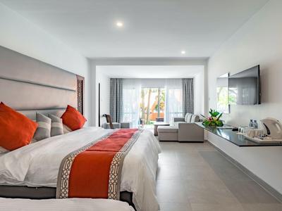 Moderní hotelový pokoj s dvojlůžkem, červenými akcenty a posezením s výhledem na terasu.