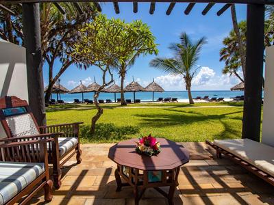 Pohled z kryté terasy do tropické zahrady s bazénem a mořem v pozadí.