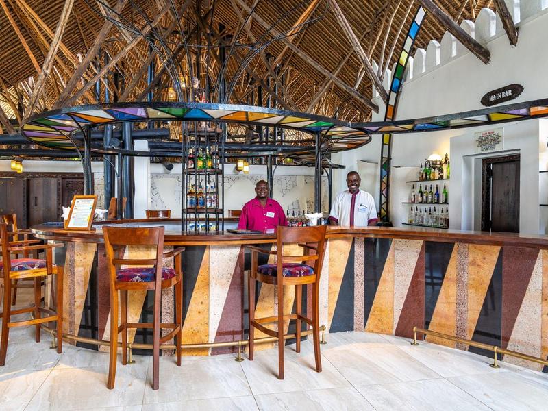 Moderní hotelový bar s dřevěnými židlemi a tropickou střechou z palmových listů.