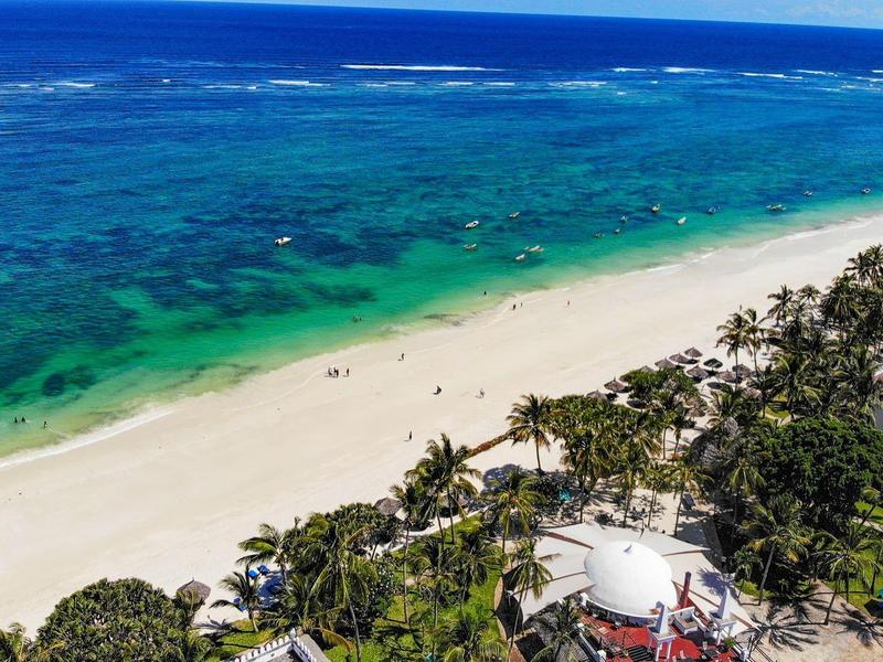 Pohled na bílou písečnou pláž s tyrkysovou vodou a palmami podél pobřeží.