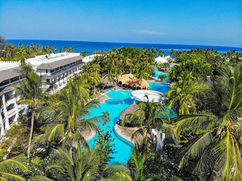 Pohled na tropický resort s několika lagunovými bazény, palmami a hotelovými budovami u moře.