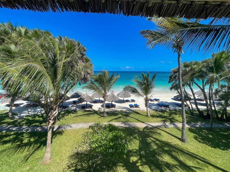 Tropická pláž s palmami, lehátky a slunečníky u jasně modrého moře.