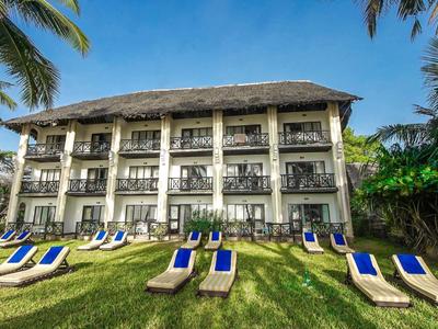 Dreistöckiges Hotelgebäude mit Holzbalustraden vor grüner Wiese und blauen Liegestühlen.