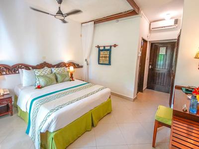 Helles Schlafzimmer mit grün-weißem Bett, Holzmöbeln, Deckenventilator und Wanddeko.