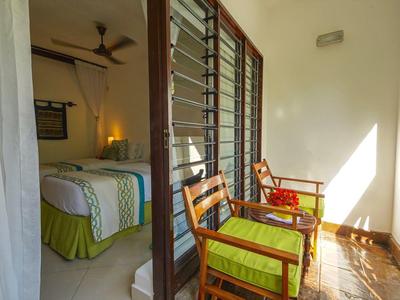 Balkon mit zwei Holzstühlen und grünen Kissen, angrenzendes Schlafzimmer mit Doppelbett.