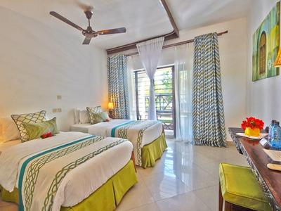 Helles Hotelzimmer mit zwei Betten, Lampen, Deckenventilator und Balkon mit Vorhängen.