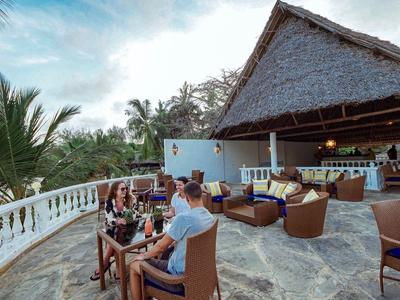 Terrassenbar mit Strohdach, Rattanmöbeln und Meerblick bei bewölktem Himmel.