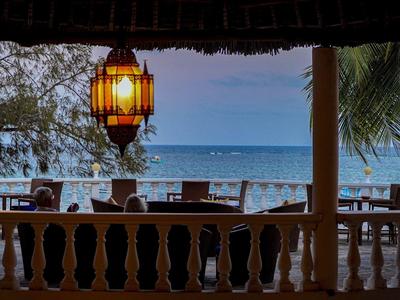 Offene Terrasse mit Holzgeländer, Lampe, Stühlen und Blick auf Meer und Himmel bei Abenddämmerung.
