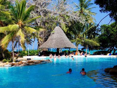 Großer blauer Pool umgeben von Palmen und einer Strohhütte unter klarem Himmel.