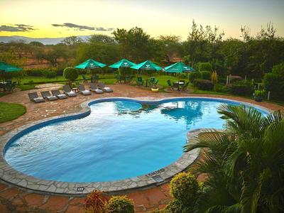 Ein geformter Swimmingpool mit Sonnenliegen und grünen Sonnenschirmen bei Sonnenuntergang.