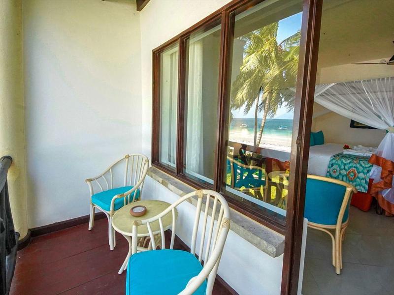 Balkon mit zwei weißen Stühlen und Tisch, Blick ins Zimmer mit Bett und Moskitonetz tropisch.