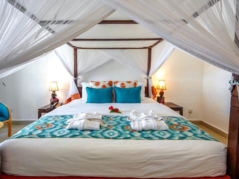 Schlafzimmer mit Himmelbett, türkisgemustertem Bettbezug und weißen Vorhängen, zwei Handtücher liegen.