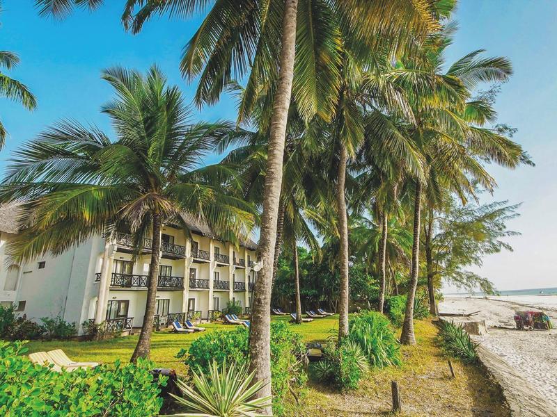 Hotel an einem tropischen Strand mit Palmen und klarem Himmel.