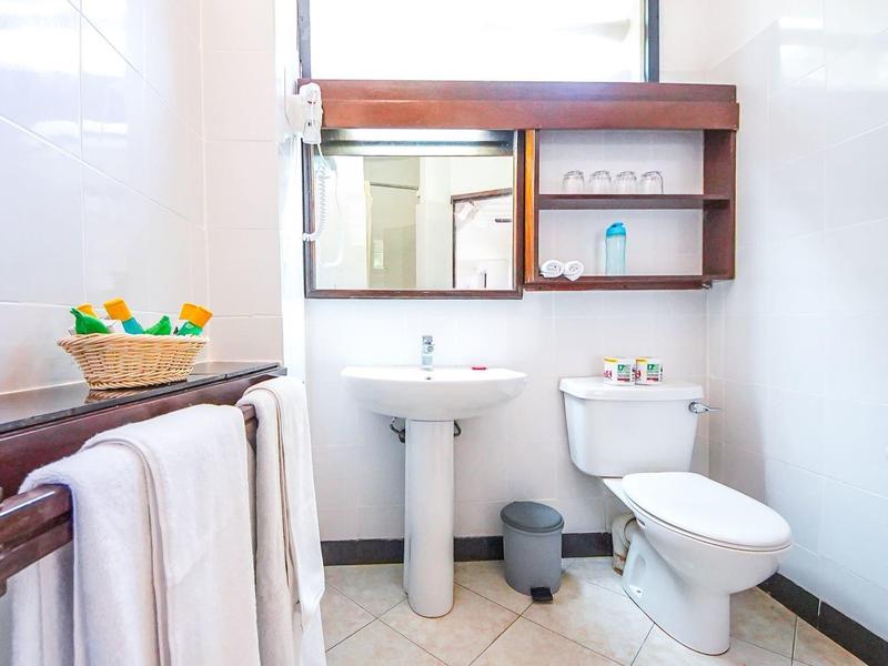 Helles Badezimmer mit weißem Waschbecken, Toilette, Handtüchern und Holzmöbeln an der Wand.