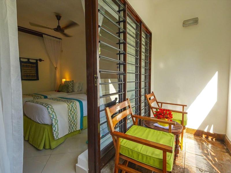 Balkon mit zwei Holzstühlen und grünen Kissen, angrenzendes Schlafzimmer mit Doppelbett.