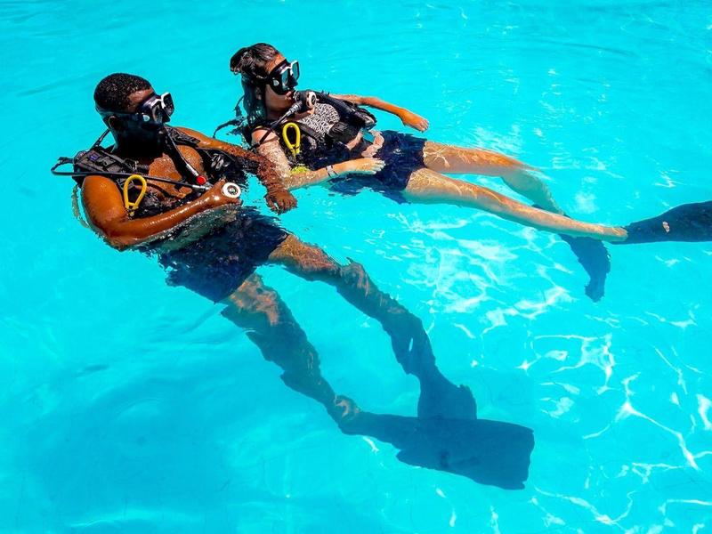 Zwei Taucher mit Ausrüstung schwimmen entspannt in klarem, blauem Wasser.