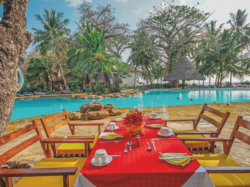 Außenrestaurant mit rot gedecktem Tisch und Blick auf einen Pool und Palmen.