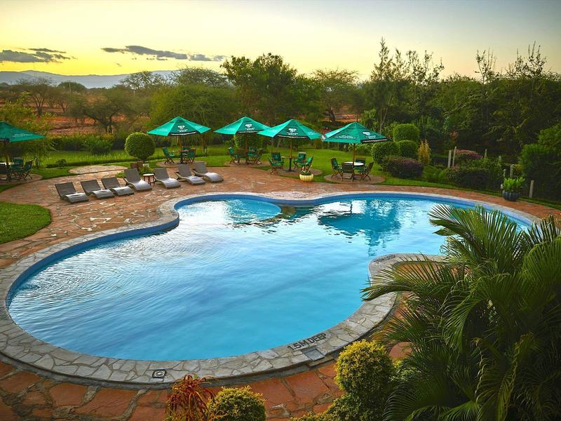 Ein geformter Swimmingpool mit Sonnenliegen und grünen Sonnenschirmen bei Sonnenuntergang.