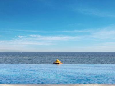 Ein Schwimmer im gelben Schwimmring im Infinity-Pool mit Meer und blauem Himmel im Hintergrund.