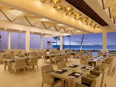 Modernes Restaurant mit Holzstühlen und Tischen mit Meerblick bei Sonnenuntergang.