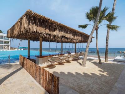 Strandnaher Ruhebereich mit Palmen und überdachten Liegen neben einem Pool.