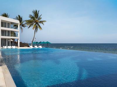 Infinity-Pool mit Blick auf das Meer neben einem weißen Hotelgebäude und Palmen.