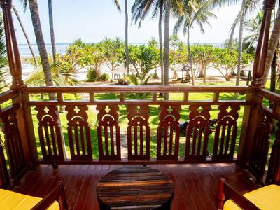 Véranda en bois avec rambarde ornée donnant sur des palmiers et un jardin tropical.