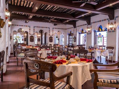 Restaurant élégant avec poutres en bois, nappes blanches et mobilier en bois foncé.