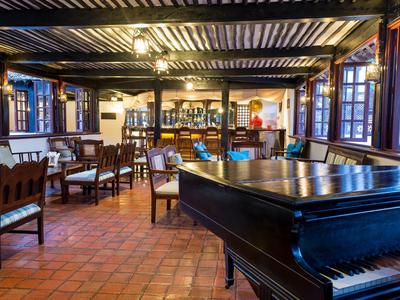 Salle à manger d'hôtel accueillante avec piano, tables en bois et chaises dans un style rustique.