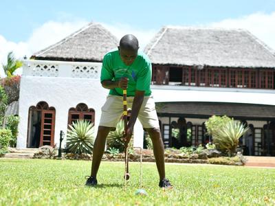 Ein Mann spielt Golf auf dem Rasen vor einem weißen, traditionell gestalteten Gebäude mit Strohdach.
