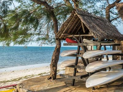 Strandhütte mit aufgereihten Surfboards unter Bäumen am Meer