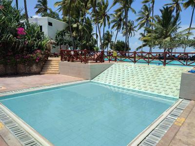 Piscine vide avec des palmiers et des bâtiments en arrière-plan sous un ciel bleu.