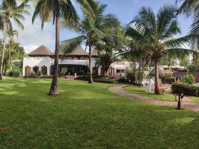 Großer Garten mit Palmen und einem Hotelgebäude im Hintergrund bei sonnigem Wetter.