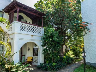 Un bâtiment blanc avec un balcon et un chemin à côté d'un grand arbre et de la végétation verte.