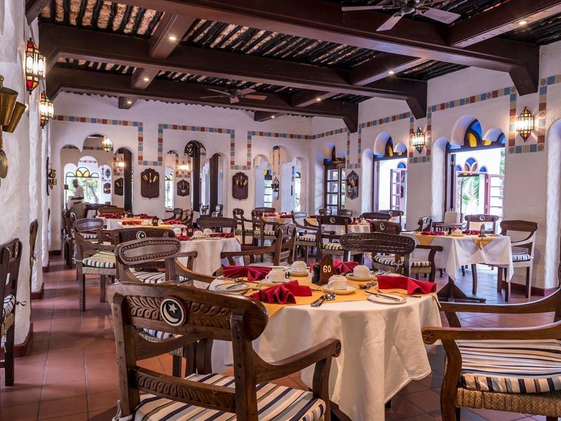 Restaurant élégant avec poutres en bois, nappes blanches et mobilier en bois foncé.
