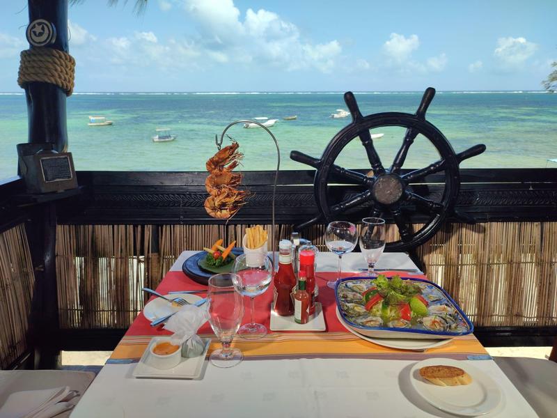 Table avec nourriture et boissons devant une roue de navire avec vue sur la mer