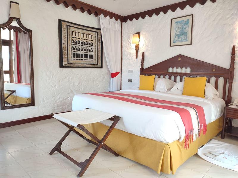 Chambre d'hôtel confortable avec lit en bois rustique, coussins colorés et décorations murales.