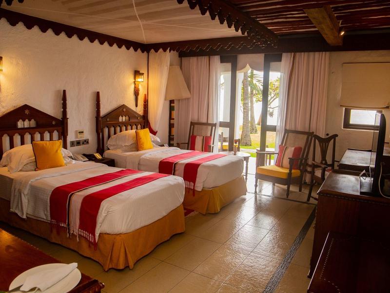 Chambre twin avec plafond en bois, deux lits, table, chaises et balcon donnant sur l'extérieur.