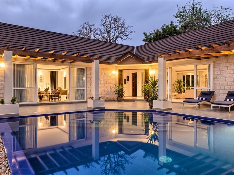 Moderní rekreační dům s osvětleným bazénem a terasou za soumraku.