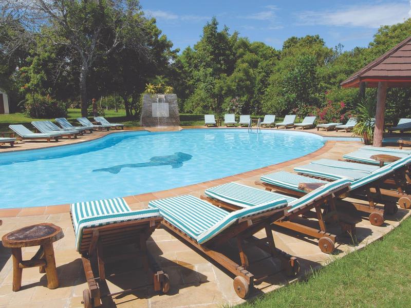 Příjemný bazén s modrými lehátky a stromy v pozadí v hotelové zahradě.