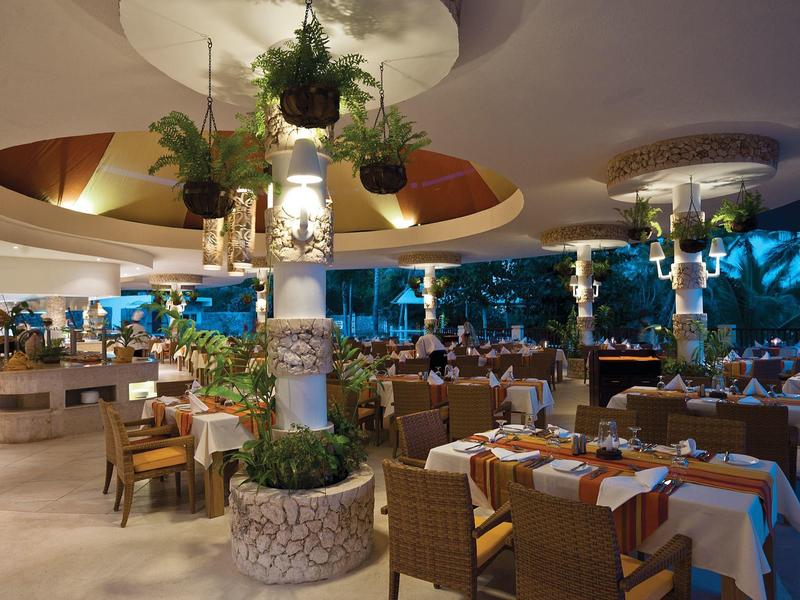 Elegantní hotelová restaurace s prostřenými stoly a závěsnými rostlinami v uvolněné atmosféře.