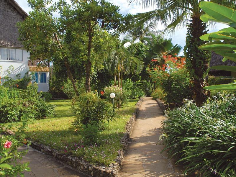 Cesta vede tropickou zahradou s palmami vedle bílého domu.