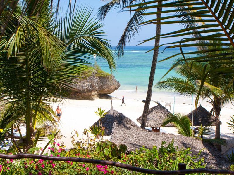 Výhled na tropickou pláž s palmami, bílým pískem a průzračnou modrou vodou.