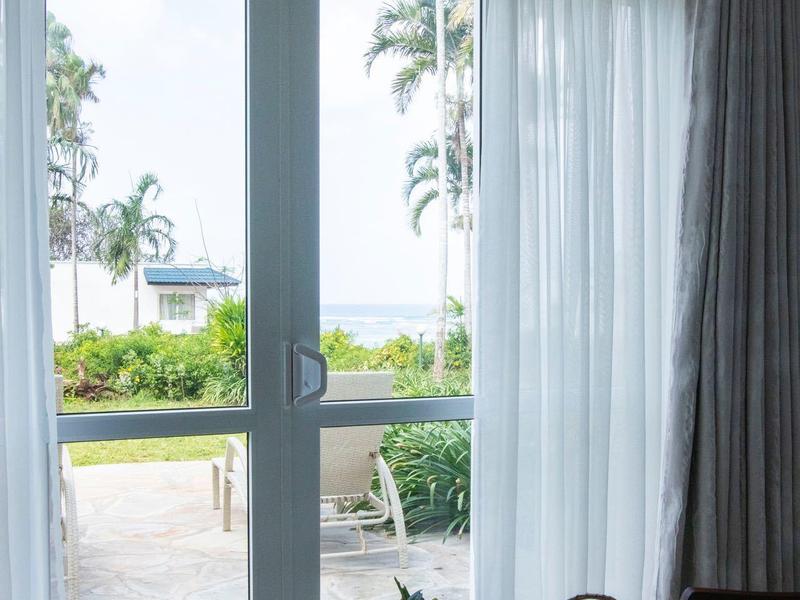 Výhled přes skleněné dveře na terasu s palmami a prostřeným stolem v popředí.