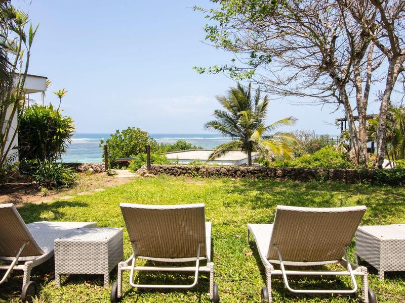 Lehátka na trávníku s výhledem na moře a palmy pod jasnou oblohou.