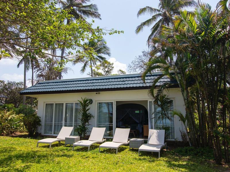 Malý rekreační dům s lehátky obklopený palmami a zeleným trávníkem.