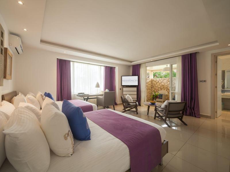 Moderně zařízený hotelový pokoj s manželskou postelí, posezením a přístupem na balkon.